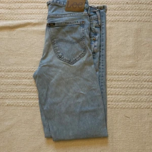 Ljusblå Lee jeans med rak passform - Säljer ett par ljusblå jeans från Lee med klassisk femficksdesign och rak passform. Jeansen har normal midja och är tillverkade i mjukt denimtyg. Perfekta för en avslappnad och stilren look.