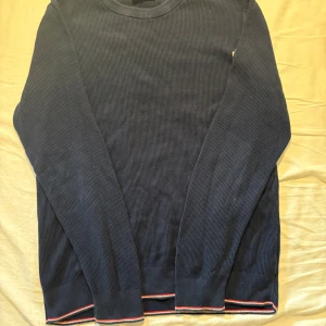 Mörkblå stickad tröja från Moncler - Säljer en mörkblå stickad tröja från Moncler i 100% bomull. Tröjan har lång ärm, rund halsringning och Moncler-logga på ryggen. Nedtill finns en snygg detalj med röd, vit och blå rand. Perfekt för dig som gillar stilrena och exklusiva plagg.