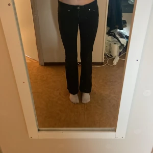 Svarta bootcut jeans från Perfect Jeans (gina tricot) - Svarta jeans från Perfect Jeans (gina tricot) i bootcut-modell med snygga fickor bak som har lock och silverfärgade knappar. Jeansen har en klassisk femficksdesign och är tillverkade i stretchigt denimtyg för en bekväm passform. Perfekta för dig som gillar en tidlös look.