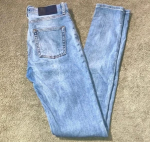 J.Lindeberg skinny jeans, storlek 28/34 - Snygga ljusblå jeans från J.Lindeberg med klassisk femficksdesign och diskret slitning framtill. Jeansen har rak passform och normal midja, tillverkade i mjukt bomullsjeansmaterial. Perfekta för dig som gillar stilrena och tidlösa jeans.