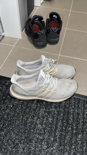 Adidas Ultraboost ljusgrå sneakers - Säljer ett par Adidas Ultraboost sneakers i ljusgrått med stickad ovandel och klassiska tre ränder på sidan. Skorna har snörning, platt sula och en mjuk, boostad mellansula för extra komfort. Perfekta för dig som gillar stilrena och sportiga sneakers.