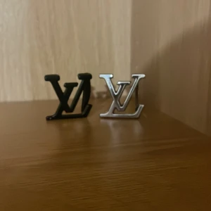 Louis Vuitton bältespännen svart & silver - Två stilrena bältespännen från Louis Vuitton, ett i mattsvart och ett i blankt silver. Båda har den ikoniska LV-loggan och är tillverkade i metall. Perfekt för att ge din outfit en lyxig touch och visa din stil.