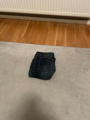 Mörkblå jeans från Nudie Jeans - Säljer ett par mörkblå jeans från Nudie Jeans med klassisk femficksdesign och snygga kontrastsömmar. Jeansen är i bomull och har en rak passform som funkar till det mesta. Perfekt för dig som gillar stilrena och tidlösa jeans.