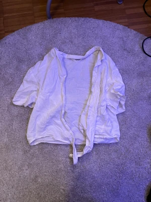 Vit linneskjorta med knyt från H&M - Vit skjorta från H&M i luftig linnemix med korta ärmar och knyt framtill. Skjortan har en avslappnad passform och är perfekt för varmare dagar. Enkel och stilren design som är lätt att matcha.