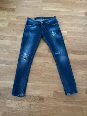 Blå skinny jeans från Dondup - Säljer ett par blå jeans från Dondup i skinny fit med slitna detaljer och snygga slitningar på benen. Klassisk femficksmodell med kontrastsömmar och låg midja. Jeansen har en cool tvätt och är perfekta för dig som gillar en modern streetstil.