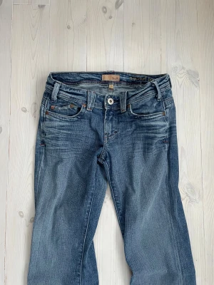 Blå bootcut jeans från YakuKi - Snygga blå jeans från YakuKi med bootcut passform och coola broderade detaljer på bakfickorna. Jeansen har sexficksdesign, kontrastsömmar och är tillverkade i slitstarkt denim. Dem har gått sönder lite där uppe som man kan se på bild 3 och 4 men det går säkert att fixa, dem är även lite upptrampade men det är inget man tänker på när man har på sig dem