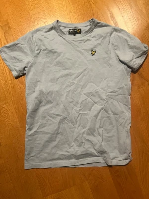 Ljusblå t-shirt från Lyle & Scott - Säljer en ljusblå t-shirt från Lyle & Scott med klassisk gul logga på bröstet. T-shirten har rund hals, korta ärmar.