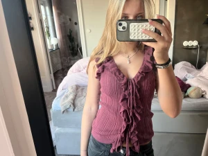 Vinröd ribbad topp med volanger från Zara - Superfin vinröd topp från Zara med ribbad struktur och volangdetaljer längs v-ringningen. Toppen är ärmlös och har snörning framtill som ger en snygg touch. Perfekt att styla med jeans eller kjol för en trendig look.