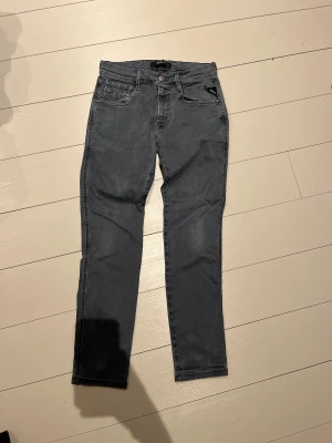 Replay grå jeans slim fit 29/32 - Snygga grå jeans från Replay i slim fit-modell. Klassisk femficksdesign med Replay-logga på bakfickan och läderpatch i midjan. Jeansen har normal passform och raka ben, tillverkade i mjukt jeansmaterial. Perfekt för dig som gillar stilrena och bekväma jeans.