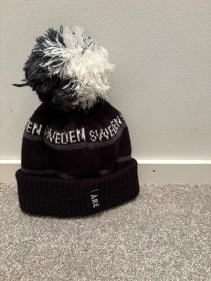 Svart och vit Åre mössa med tofs - Snygg svart och vit mössa med stor fluffig tofs på toppen. Ribbad kant för extra komfort. Perfekt för kalla dagar och vinterhäng. Det är en väldigt skön och snygg vintermössa. Jag har använt den 1-2 gånger och pris går att diskutera. 