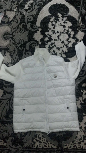 Vit Moncler pufferjacka med stickade ärmar - Säljer en clean vit pufferjacka från Moncler med stickade ärmar och hög krage. Jackan har dragkedja, två fickor med knapp och Moncler-logga på bröstet. Insidan har en cool serietidningsetikett. Perfekt för dig som vill ha en snygg och modern look.