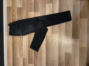 Svarta jeansbyxor i storlek 28/32 - Snygga svarta jeansbyxor med klassisk femficksdesign och smal passform. Jeansen har en mörk tvätt och raka ben, vilket ger en stilren look. Perfekt för dig som gillar en enkel och clean stil. Materialet är slitstarkt jeans och midjan är normal.