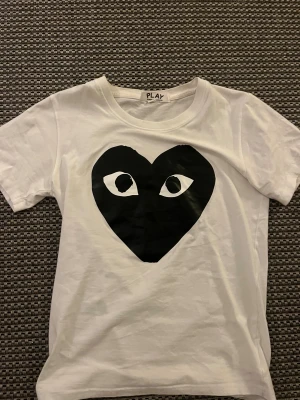 Vit Comme des Garçons Play t-shirt - Vit t-shirt från Comme des Garçons Play med det ikoniska svarta hjärtat med ögon tryckt på bröstet. Klassisk rund halsringning och korta ärmar. Tillverkad i mjuk bomull för en skön känsla och clean look.