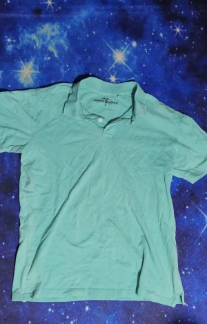 Turkos pikétröja från Hampton Republic - Snygg turkos pikétröja från Hampton Republic med klassisk krage och två knappar vid halsen. Tröjan är i bomull och har korta ärmar, perfekt för en avslappnad och stilren look.