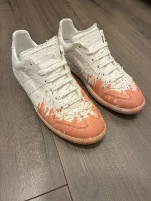 Maison Margiela sneakers stl 40 - Maison Margiela sneakers i vit med färgstänk på. Säljer för att det här inte riktigt är min stil längre! Box osv medföljer! Använd några fåtal gånger!