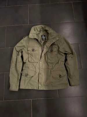 Fieldjacka från Superdry - Säljer en grön fieldjacka från Superdry, modell Rookie Field. Mycket bra skick, bara använt ett fåtal gånger. Storlek XS men stor i storlek