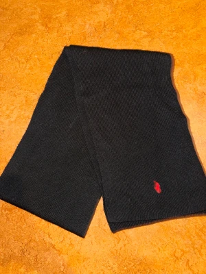 Ralph Lauren halsduk - Säljer denna svarta och snygga Ralph Lauren halsduken som är lite mindre i storlek men perfekt för en wrap around runt halsen nu under vintern.