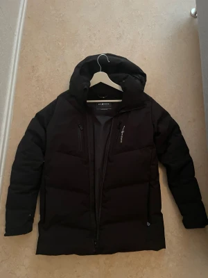 Svart dunjacka från Sail Racing - Svart dunjacka från Sail Racing.Kommer hålla dig riktigt varm. Den ser sliten ut på baksidan men de är pågrund av ljuset. Kan också sänka priset pågrund av skadorna vid båda armen 