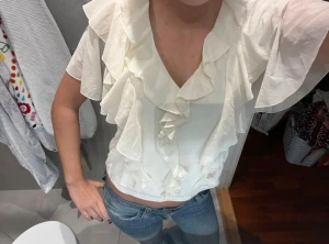 Vit blus med volanger och v-ringning - Säljer en superfin vit blus med v-ringning och stora volanger framtill och runt axlarna. Blusen är lätt transparent och har korta, luftiga ärmar.