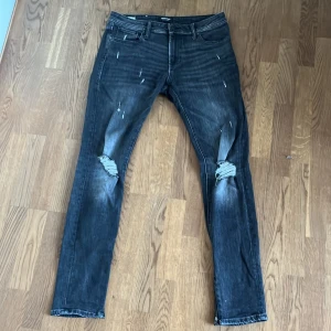 Jack & Jones svarta slim jeans - Säljer ett par svarta skinny jeans från Jack & Jones med slitna detaljer och slitningar vid knäna. Jeansen har en cool tvättad look och är gjorda i stretchigt denim. Det är bara att höra av sig vid fler frågor🙌🏻 priset är ej hugget i sten!