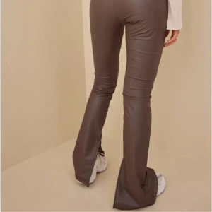 Bruna bootcut byxor i skinnimitation - Snygga bruna bootcut byxor i skinnimitation med hög midja och slits vid benslutet. Byxorna har en tight passform upptill och vida ben nertill. 