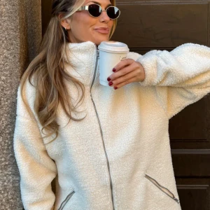 Krämvit teddyjacka  - Mysig teddyjacka i krämvit färg med hel dragkedja framtill och två snedställda fickor med dragkedja. Jackan har hög krage och är tillverkad i fluffigt fleece-material. Perfekt för kalla dagar och ger en chill vibe. Nypris: 1299kr