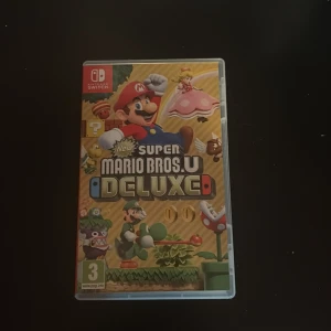 New Super Mario Bros. U Deluxe - New Super Mario Bros. U Deluxe till Nintendo Switch i mycket fint skick. Komplett med originalfodral och spelkassett. Ett klassiskt Mario-plattformsspel med över 160 banor och stöd för upp till 4 spelare. Perfekt för familj och vänner!
