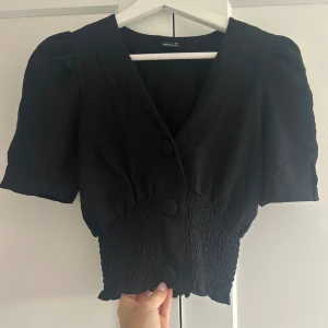 Svart blus - Säljer en svart blus från Gina med en v-ringning och stora knappar framtill. 