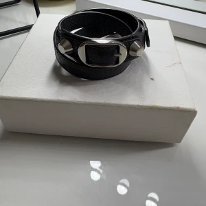 Balenciaga grått läderarmband - Grått Balenciagaarmband som är köpt på vestiaire. Inga defekter. Tillhörande box och påse medföljer.