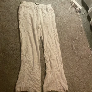 Vita vida linnebyxor med resår - Säljer ett par vita linnebyxor med resår i midjan och raka, vida ben. Byxorna har en avslappnad passform och är perfekta för varma dagar. Lätta och luftiga med enkel design, passar dig som gillar stilren och chill vibe.