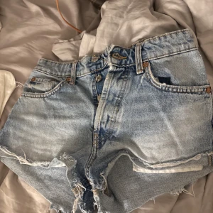 Ljusblå jeansshorts från Zara - Snygga ljusblå jeansshorts från Zara med hög midja och råa, fransiga kanter. Klassisk femficksmodell med knappgylf och slitna detaljer för en avslappnad vibe. Perfekta till sommaren och lätta att matcha med allt.