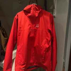 Röd vindjacka från Haglöfs, M - Säljer en röd vindjacka från Haglöfs i storlek M. Jackan har huva, lång ärm och en smidig half zip framtill. Materialet är lätt och syntetiskt, perfekt för utomhusaktiviteter. Snygg minimalistisk design med Haglöfs-logga på bröstet.