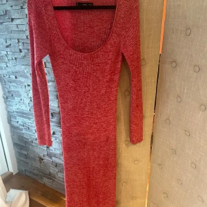 Röd ribbad långklänning från MNG - Snygg röd långklänning från MNG med ribbat mönster och lång ärm. Klänningen har en djup rundad urringning och är figurnära i modellen. Perfekt för dig som gillar en enkel men ändå iögonfallande stil.Helt ny