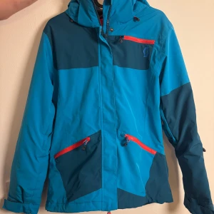 Blå skidjacka från Scott  - Säljer en blå och mörkblå skidjacka från Scott med röda dragkedjor. Jackan har flera fickor med dragkedja. Funkar även superbra som vinterjacka.