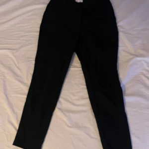 Svarta kostymbyxor med smal passform - Snygga svarta kostymbyxor med smal passform och klassisk design. Byxorna har hällor för bälte och raka ben som smalnar av nedtill. Perfekta för en stilren look och passar till skjorta eller t-shirt.