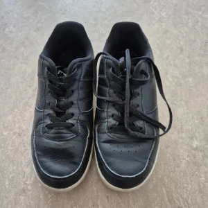 Sneakers - Svarta sneakers från Nonation i storlek 38. Skorna har klassisk design med snörning, rund tå och vit sula. Ovandelen är i syntetmaterial med diskreta sömmar och detaljer. Perfekta för en avslappnad och stilren look.