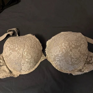 Beige spetsig bandeau tubtopp - Snygg beige bandeau tubtopp med vacker spets och blommigt mönster. Toppen är vadderad och har axelband som går att justera. Perfekt för att ge en feminin touch till din outfit. 