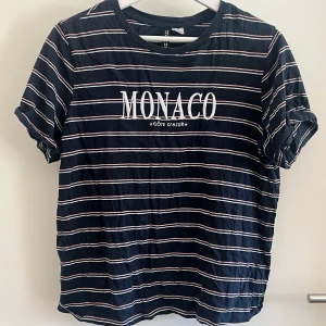 Randig t-shirt från H&M Divided - Snygg marinblå t-shirt med vita och rosa ränder från H&M Divided. Tryck med texten 'MONACO Côte d'Azur' på bröstet. Klassisk rund hals och korta ärmar. 