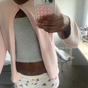 Ljusrosa kofta med knapp framtill - Supersöt ljusrosa kofta med rund halsringning och en enkel knapp framtill. Koftan har långa ärmar och är stickad i ett mjukt material. Perfekt att slänga över en topp för en chill look.