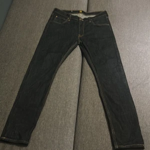 Mörkblå Lee Luke jeans W32 L30 - Säljer ett par mörkblåa Lee Luke jeans med klassisk femficksdesign och kontrastsömmar. Modellen har rak passform och normal midja, tillverkade i slitstarkt bomullsjeansmaterial. Perfekt för dig som gillar stilrena och tidlösa jeans.