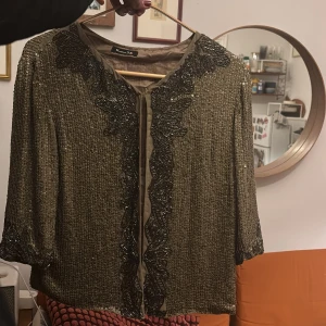 Glittrig kofta  från Massimo Dutti - Säljer en glittrig kofta från Massimo Dutti i mörkbeige med paljettbroderier och pärldetaljer längs kanterna och axlarna. Den är lite tyngre då de är äkta metall paljetter.  Jackan har trekvartsärm och öppen front, perfekt för att lyfta vilken outfit som helst.