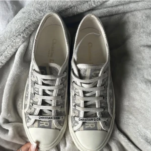 Christian Dior grå monogram sneakers - Snygga sneakers från Christian Dior i grått och vitt med ikoniskt monogrammönster. Skorna har snörning, rund tå och platt sula med stjärndetalj undertill. Passar mig som har 38!!