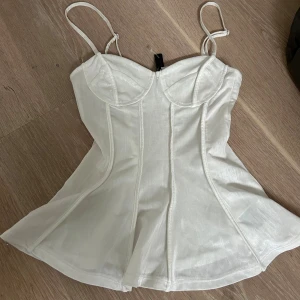 Vit korsett-topp med tunna axelband - Supersnygg vit korsett-topp från HM med tunna axelband och markerade sömmar framtill. Toppen har lätt utsvängd nederdel och smockad rygg för extra komfort. Produceras inte längre! Passar strl xxs-s då materialet är stretchigt