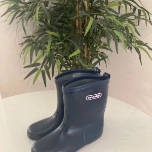 stövlar från Monship str 32-34 - Snygga mörkblå stövlar från Monship med rund tå och platt sula. Tillverkade i syntetmaterial som tål regn och rusk. Diskret logga i vitt och rosa på sidan. Perfekt för dig som vill ha stilrena boots med enkel design.