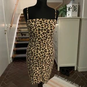 Leopardmönstrad tight kortklänning - Snygg leopardmönstrad kortklänning med smala axelband och figurnära passform. Klänningen har beige botten med svarta och bruna leopardfläckar. Materialet känns mjukt och följsamt mot kroppen.