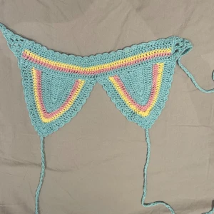 virkad topp i pastell - Superfin virkad topp med snörning i sidorna. Färgerna är ljusblå, ljusrosa och ljusgul i ett randigt mönster. Materialet känns mjukt och är stickat för en unik look.