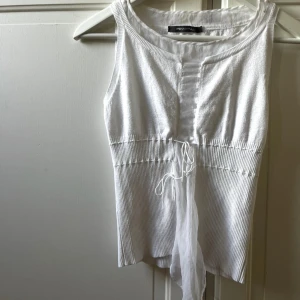 Vit ribbad linnetopp från Pennypull - Säljer en fräsch vit linnetopp från Pennypull med ribbad struktur och snygga snörningsdetaljer framtill. Toppen är ärmlös och har en lätt croppad passform med mjukt material som sitter skönt mot kroppen. Perfekt för sommarens alla tillfällen!