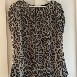 Leopardmönstrad blus från Luxus - Säljer en snygg blus från Luxus i leopardmönster med beige och svarta toner. Blusen är ärmlös och har en rund halsringning. Materialet är 100% polyester, vilket gör den lätt och skön att bära. Perfekt för dig som gillar djurmönster och vill sticka ut.