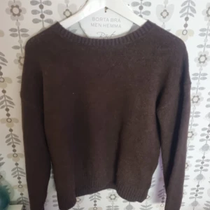 Mörkbrun stickad tröja med rund hals - En enkel och stilren mörkbrun stickad tröja med rund hals och långa ärmar. Tröjan har ribbade muddar vid ärmslut och nederkant, perfekt för att hålla värmen under kyliga dagar. Passar dig som gillar klassisk och avslappnad stil.