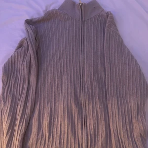 Grå ribbad kofta från Dressmann - Säljer en grå ribbad kofta från Dressmann i storlek 4XL. Tröjan har dragkedja framtill och en hög krage som ger en chill vibe. Materialet är stickat och känns mjukt mot huden. Perfekt för dig som gillar oversized och bekvämt.